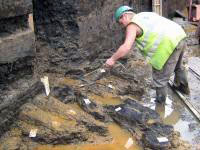 Archaeologist cleaning part of the timber trackway found at Belmarsh. Photo courtesy University College, London.